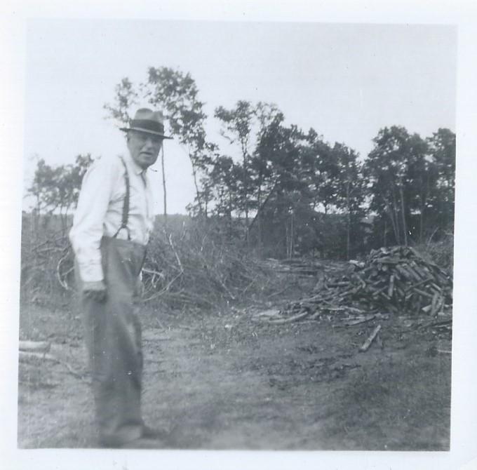 Black and white photograph of Charles Erwin Porter standing in field beside a large pile of chopped down trees.