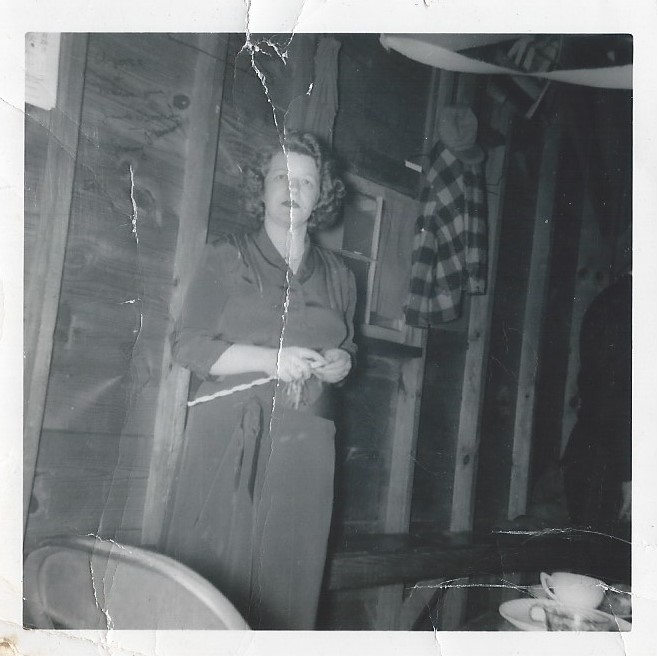 Black and white photograph of Crystal Porter standing in a rustic room with visible planks and studs.